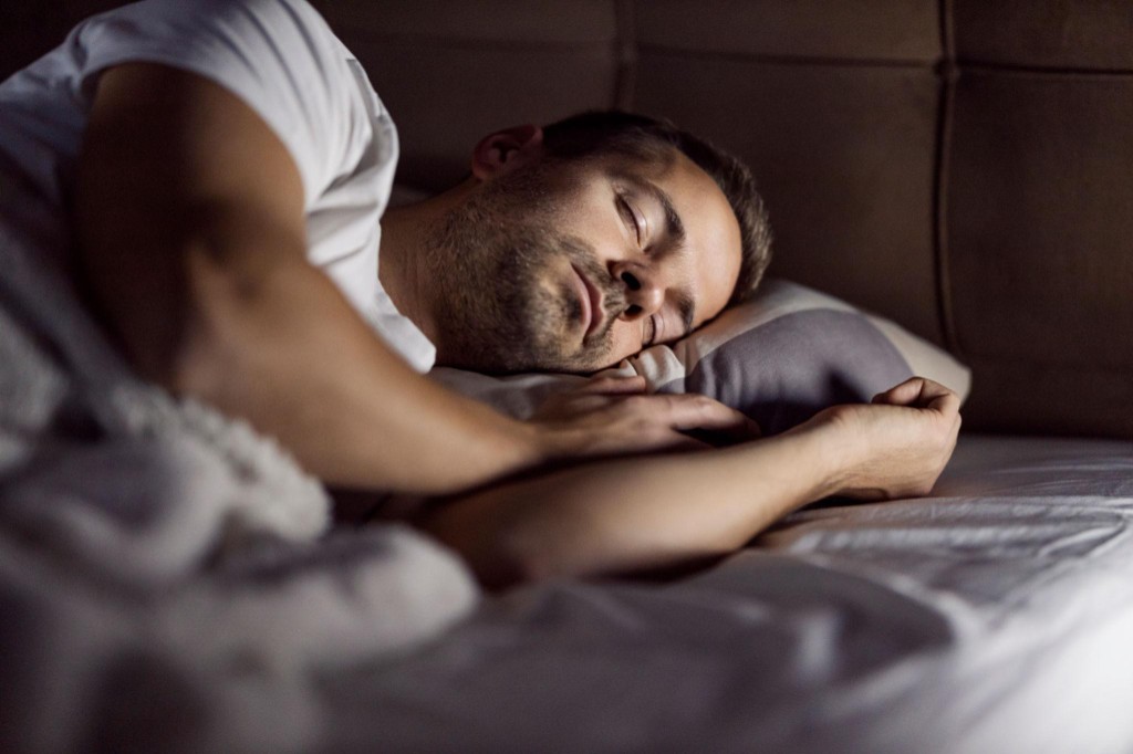 Mann Anfang 40 schläft ruhig und entspannt im Bett mit weichem Licht